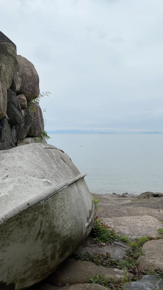 （左）蔵の脇の小道。抜けた先が湖岸です／（右）石積みの上に伏せられた小舟と、琵琶湖。対岸の山まで見えます